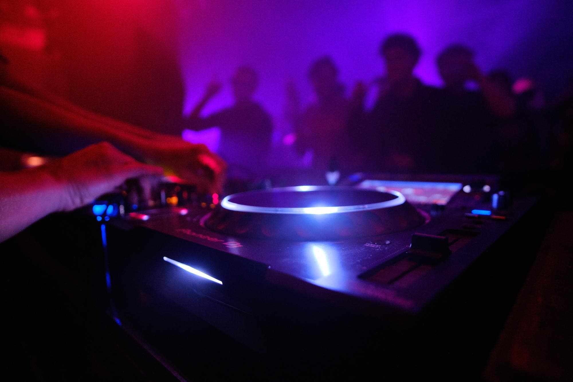 Dłonie DJ-a przy konsolecie w klubowym oświetleniu